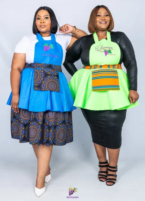 Two women wearing aprons, one blue with a mandala-print pocket and one lime green with a striped pocket