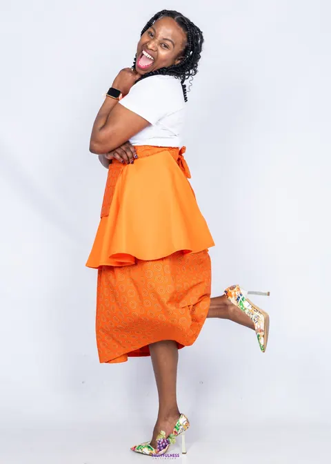 A woman laughing in an orange apron and orange print skirt, one heel kicked up