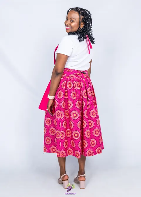 A woman smiling over her shoulder, showing how the pink apron ties at the back over its flower-print skirt