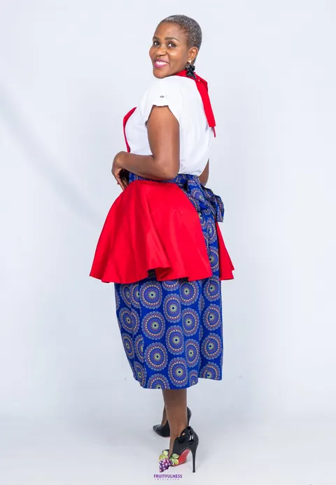 A woman smiling over her shoulder, showing the bow of the red apron tied over its blue mandala-print skirt