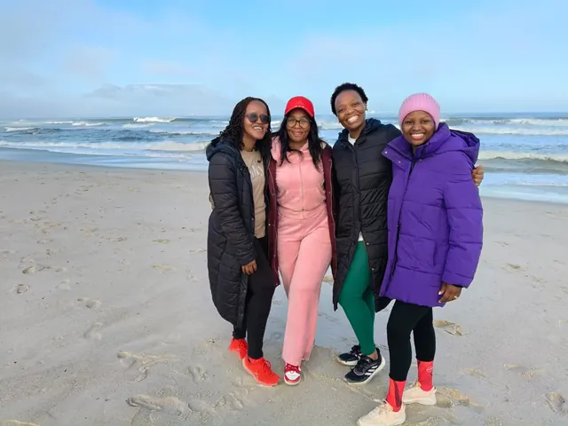Four women in warm jackets smiling together on a beach